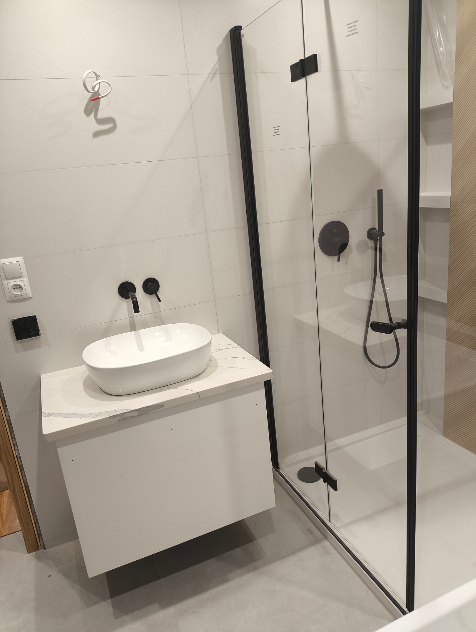 Nowoczesna łazienka z umywalką nablatową na szafce z marmurowym blatem i kabiną prysznicową z czarnymi profilami, minimalistyczny design, białe płytki.