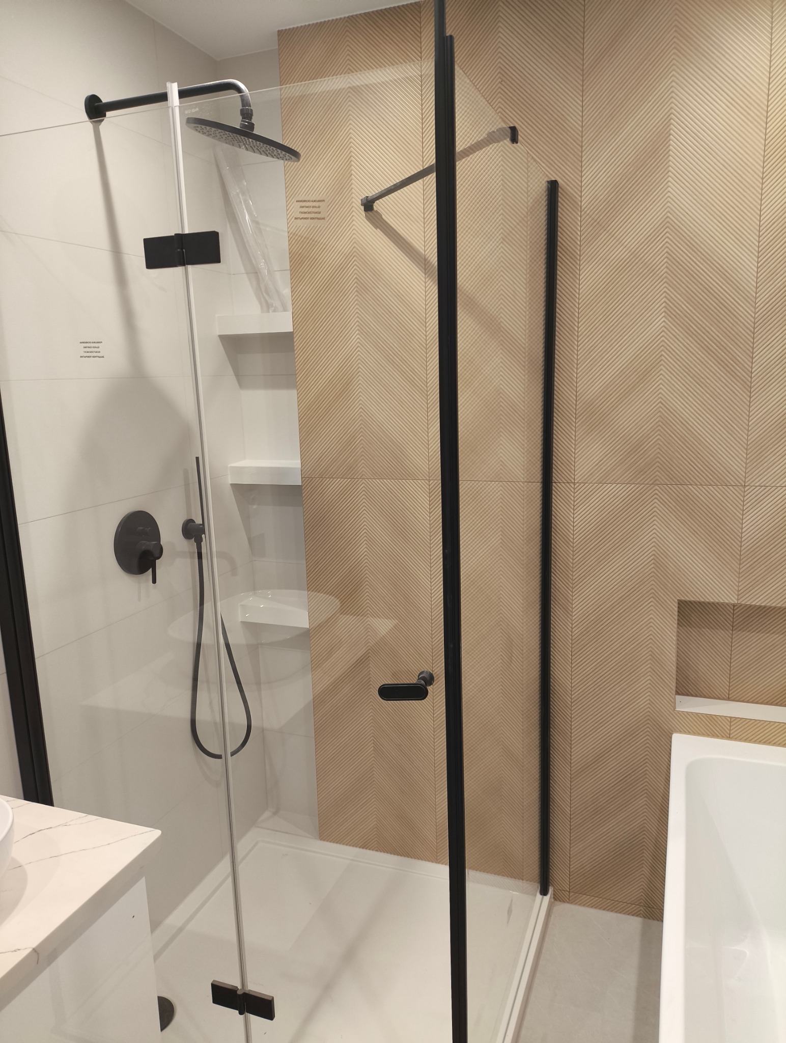Nowoczesna kabina prysznicowa z czarnymi elementami w Janowcu. Szklana ścianka, deszczownica z folią ochronną. Dekoracyjne płytki na ścianie.