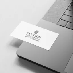 Wizytówka 'Centrum Bezpieczeństwa i Detektywistyki' leży na szarym laptopie, ukazując logo z odciskiem palca i czcionkę bezszeryfową. Minimalistyczny design.