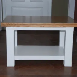 Drewniany stolik kawowy z blatem w odcieniach brązu i białymi nogami, ustawiony na ciemnej podłodze, na tle białych drzwi.