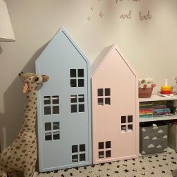 ZURFAM Wojciech Żurawiński - Dwa domki-półki w pastelowych kolorach (różowy i błękitny) w pokoju dziecięcym, obok lampa i pluszowa żyrafa. Oryginalne meble na książki i zabawki.