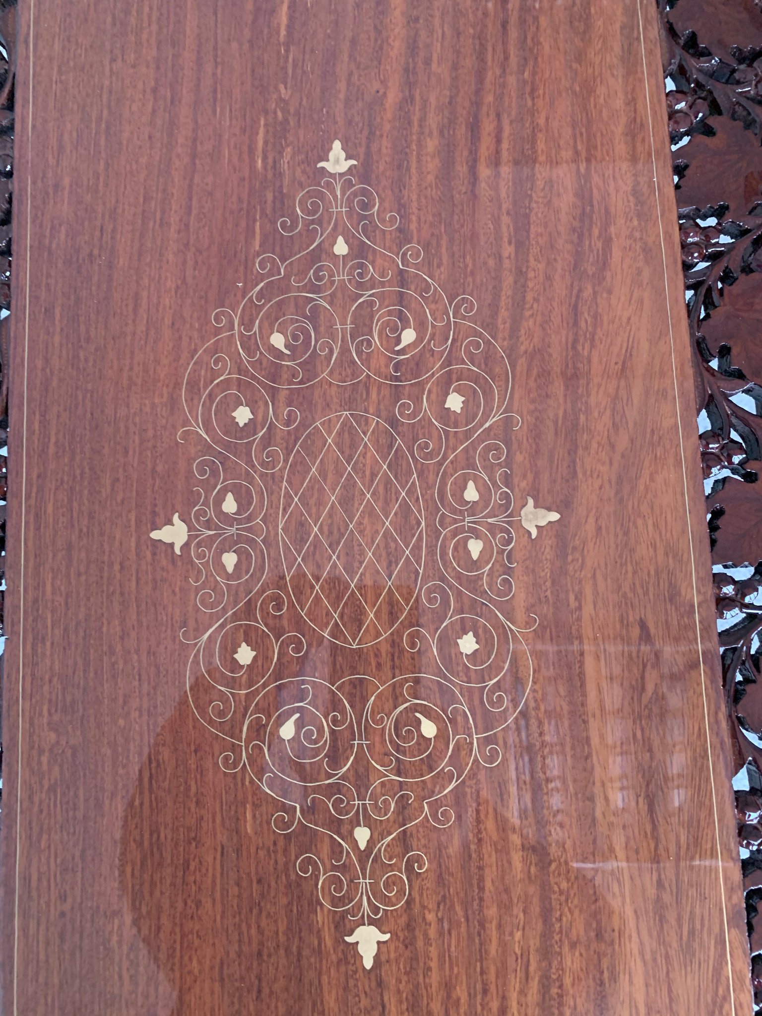 Drewniana powierzchnia stołu z intarsją w postaci ornamentu roślinnego i geometrycznego. Wykończenie na wysoki połysk. Dekoracyjny brzeg stołu.