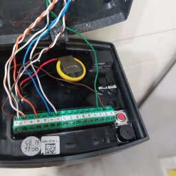 Krystian Russek - Otwarta obudowa automatu z widocznymi przewodami, zieloną listwą zaciskową, baterią i elementami elektroniki. Widoczne oznaczenia na obudowie.