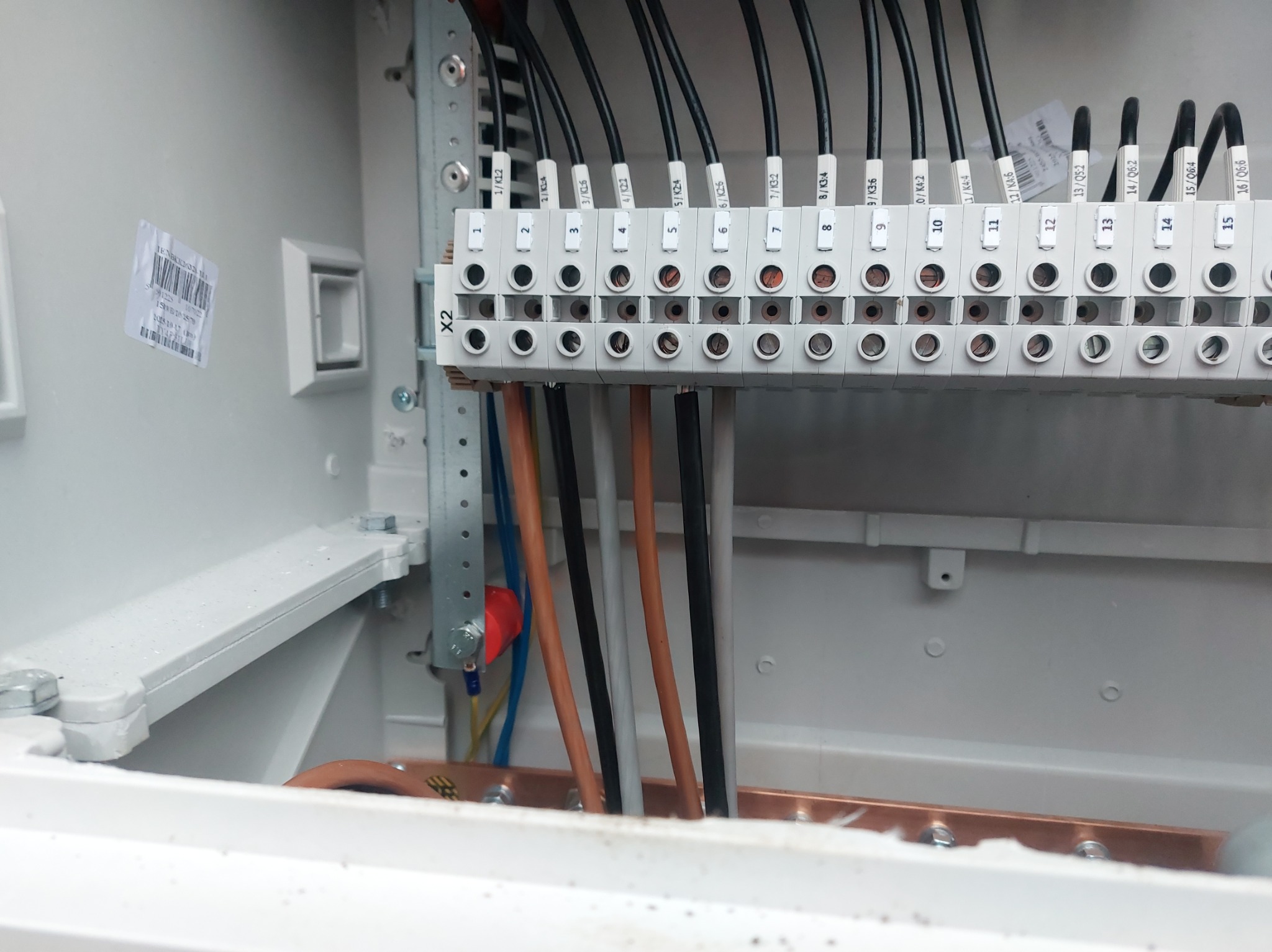 Rozdzielnica elektryczna z podłączonymi przewodami o różnych kolorach, oznaczona numerami i symbolami, widok z bliska wewnątrz skrzynki.