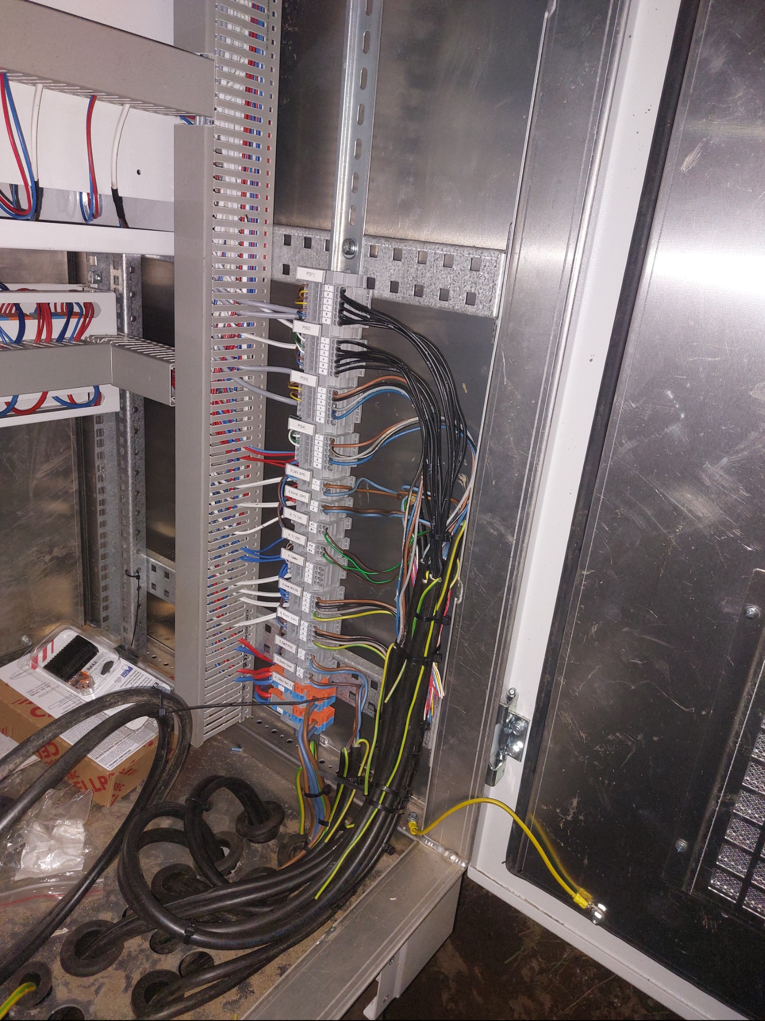 Rozdzielnica elektryczna w trakcie montażu: widoczne kable, listwy zaciskowe i metalowa obudowa. Detaliczne ujęcie na etapie łączenia przewodów.