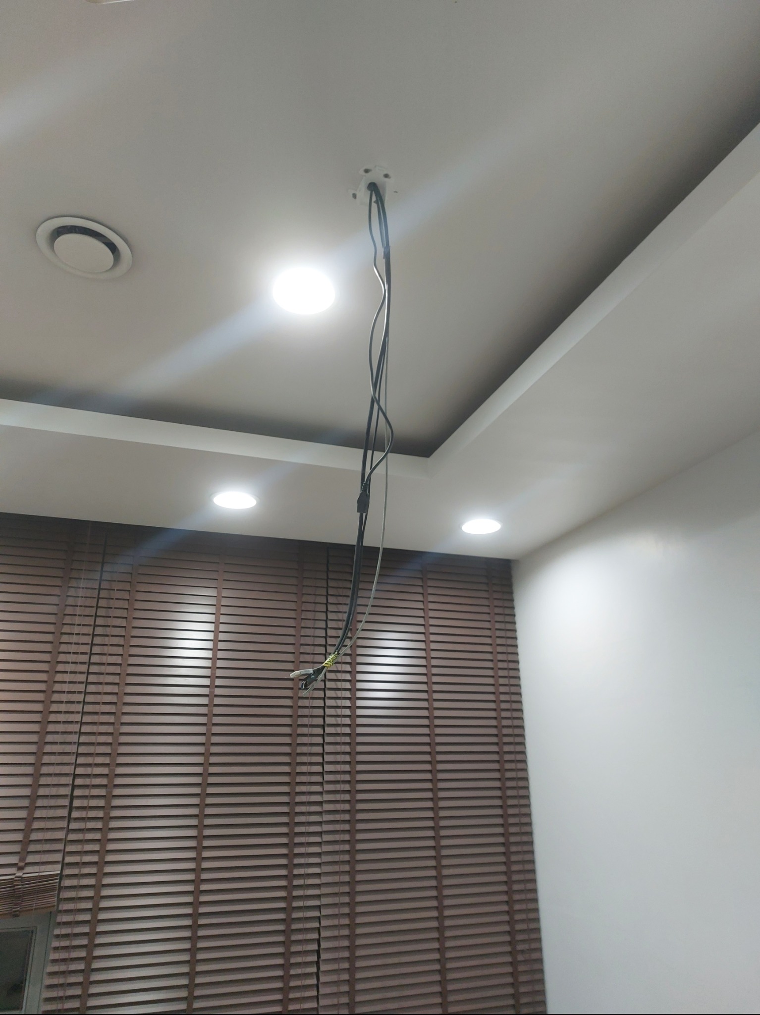 Biały sufit z trzema punktami świetlnymi, z których zwisają kable. W tle brązowe żaluzje i biała ściana. Widok z dołu, wnętrze w trakcie prac.