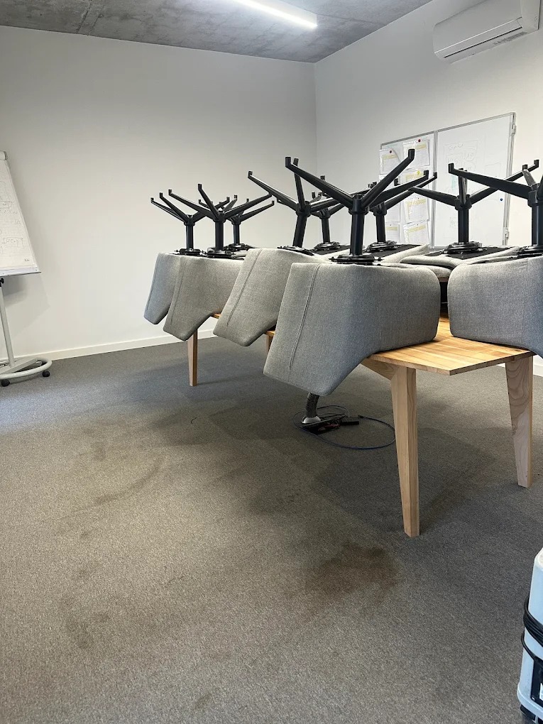 Sala konferencyjna po czyszczeniu wykładziny. Krzesła na stołach, widoczne plamy usunięte, odświeżona powierzchnia, sprzęt do czyszczenia w tle.