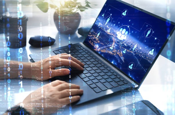 Praca na laptopie z nakładką cyfrową: dłonie na klawiaturze, na ekranie grafika sieci społecznościowej nad mapą miasta, w tle roślina doniczkowa i kubek.