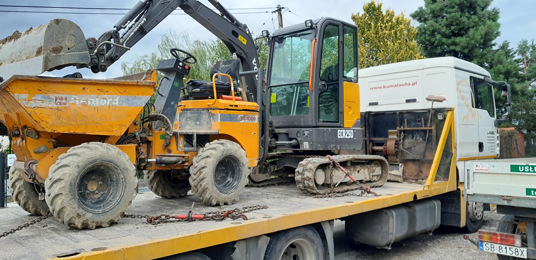 Transport koparki i wywrotki Renford na lawecie. Żółte maszyny budowlane zabezpieczone łańcuchami. Widoczny fragment kabiny ciężarówki.