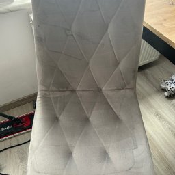 Pablo Pracz - Tapicerowane krzesło z wzorem w romby, widoczne zabrudzenia na tkaninie przed czyszczeniem. Obok podłoga i fragment urządzenia czyszczącego.