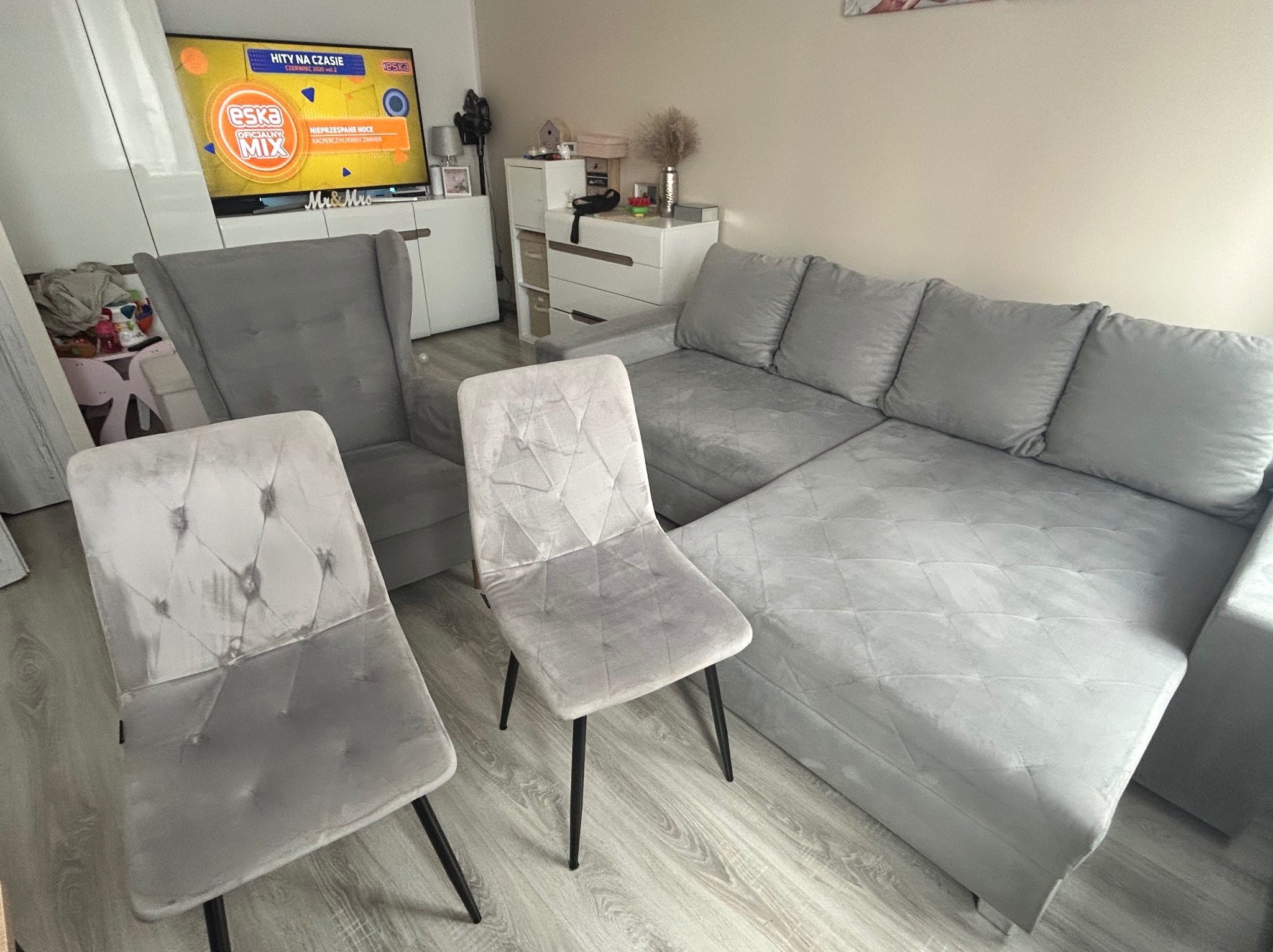 Szary narożnik, fotel i krzesła po czyszczeniu. Widoczne jaśniejsze plamy po praniu na tapicerce krzeseł. Telewizor w tle.