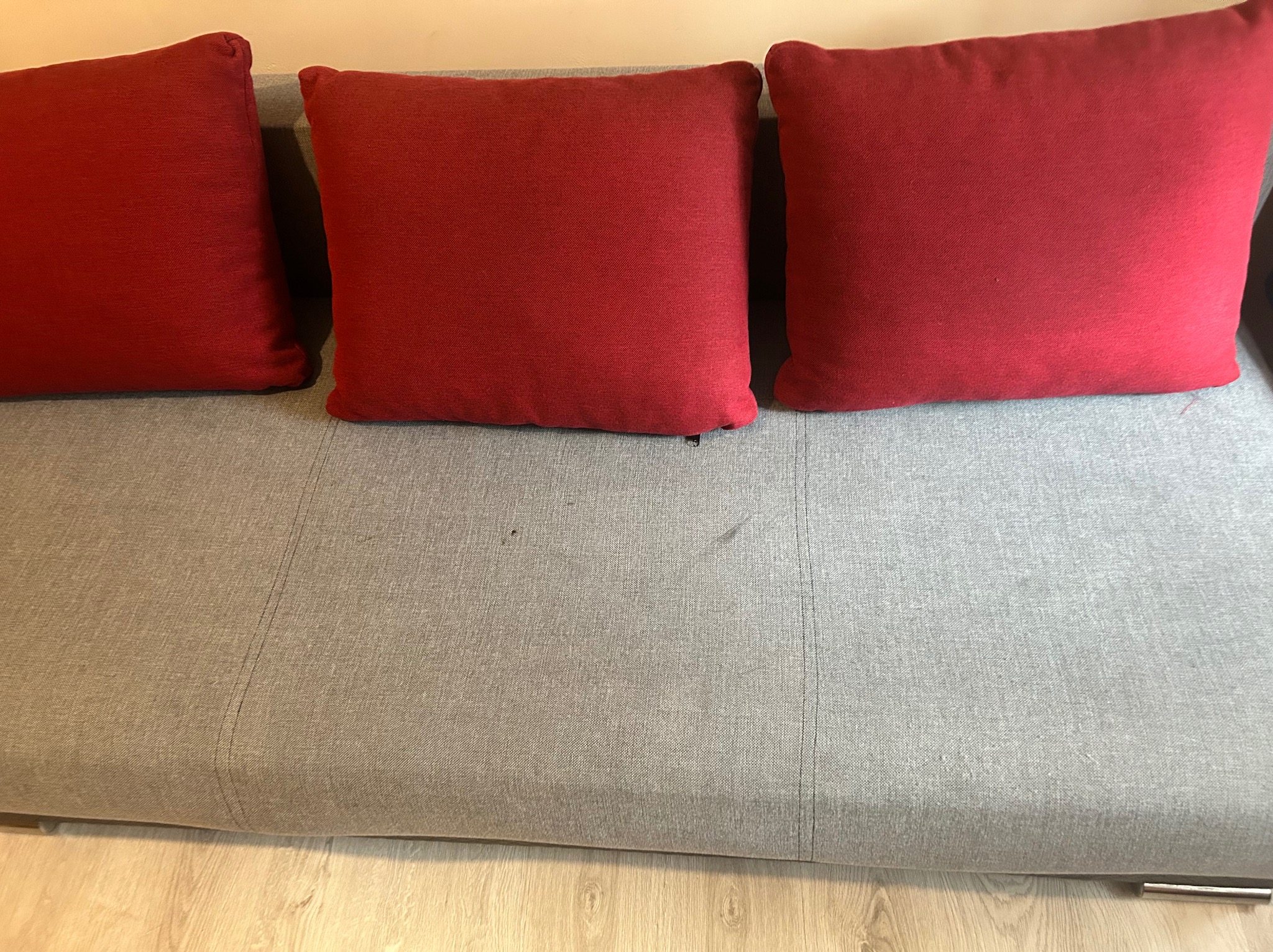 Szara kanapa z trzema czerwonymi poduszkami. Widoczne plamy na siedzisku. Zdjęcie 'po' czyszczeniu, ukazujące efekt końcowy usługi.