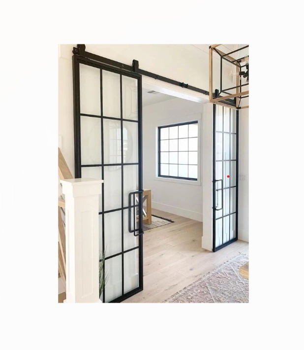 Nowoczesne, przesuwne drzwi loftowe z czarnymi szprosami i szkłem, zamontowane w jasnym wnętrzu z drewnianą podłogą i dywanem. Minimalistyczny design.