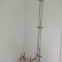 Simply Green Dorota Cierniewska - Białe przewody klimatyzacji zamocowane w ścianie za pomocą metalowych uchwytów. Instalacja w trakcie montażu, widoczne ślady po kuciu.