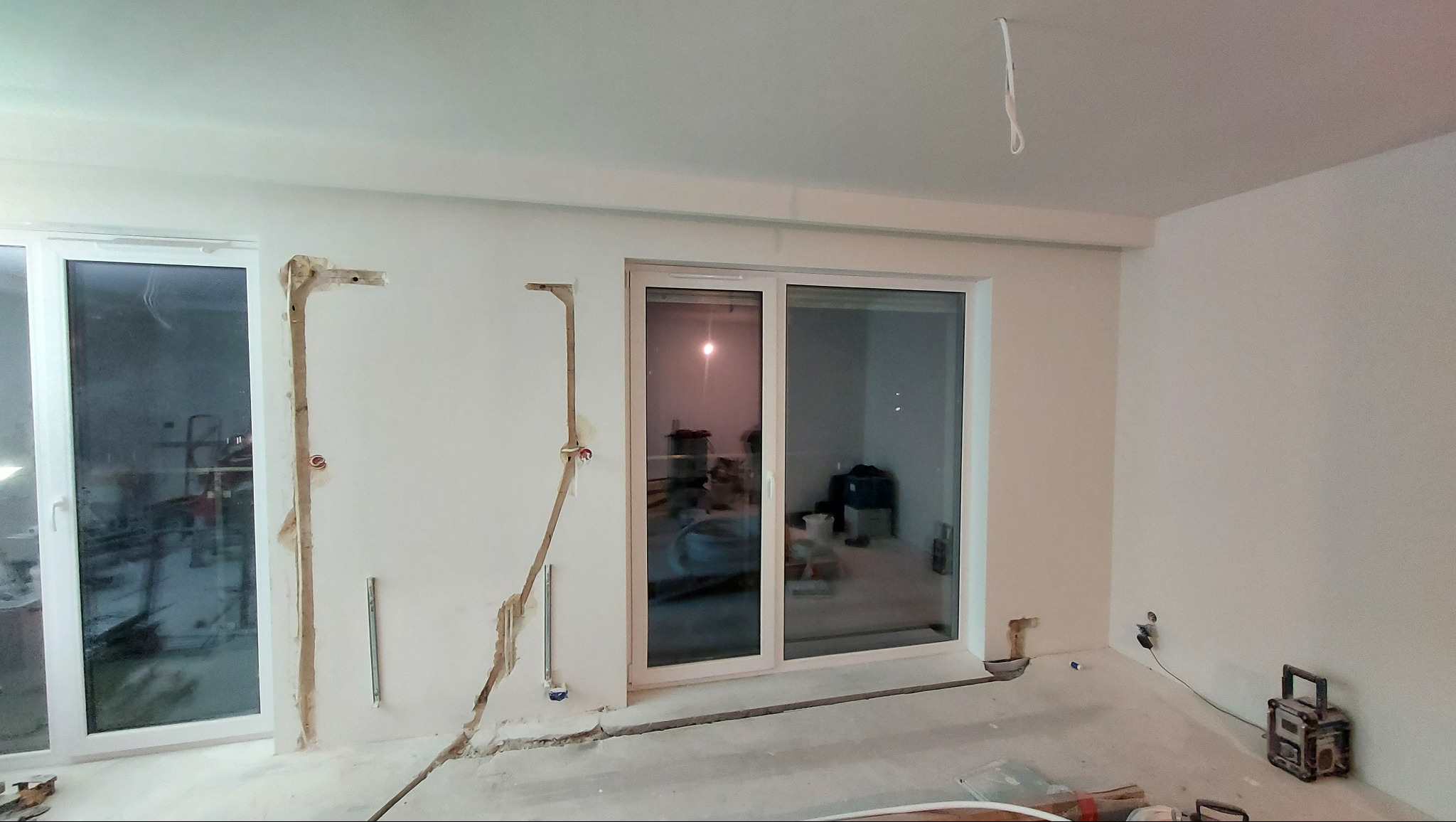 Przygotowanie instalacji pod klimatyzację w pomieszczeniu z oknami balkonowymi. Widoczne bruzdy w ścianach i wystające rurki instalacyjne. Stan surowy przed wykończeniem.