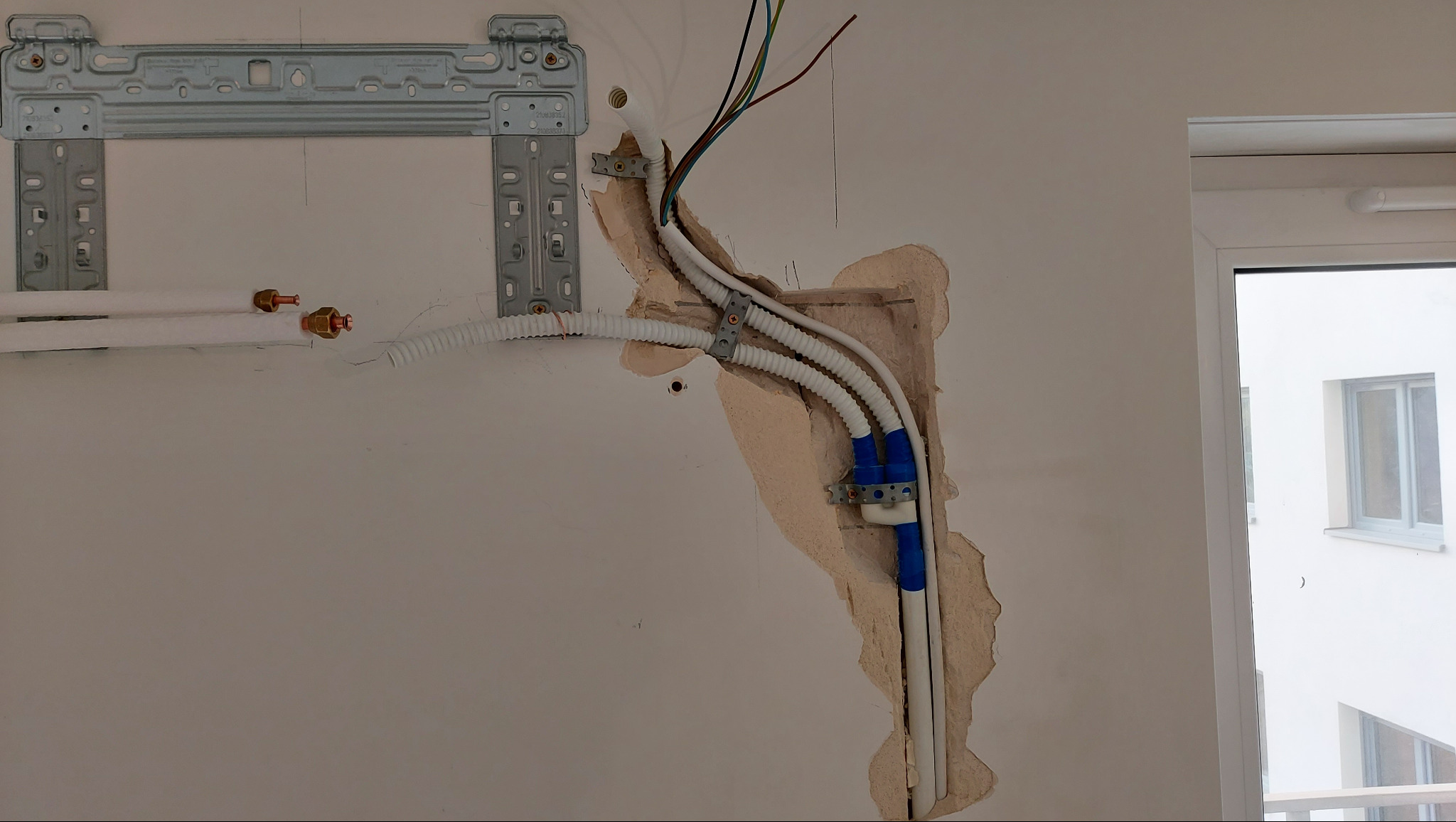 Montaż klimatyzacji: widok na ścianę z instalacją, rurami w izolacji i przewodami elektrycznymi. Metalowy wspornik jednostki wewnętrznej zamocowany.