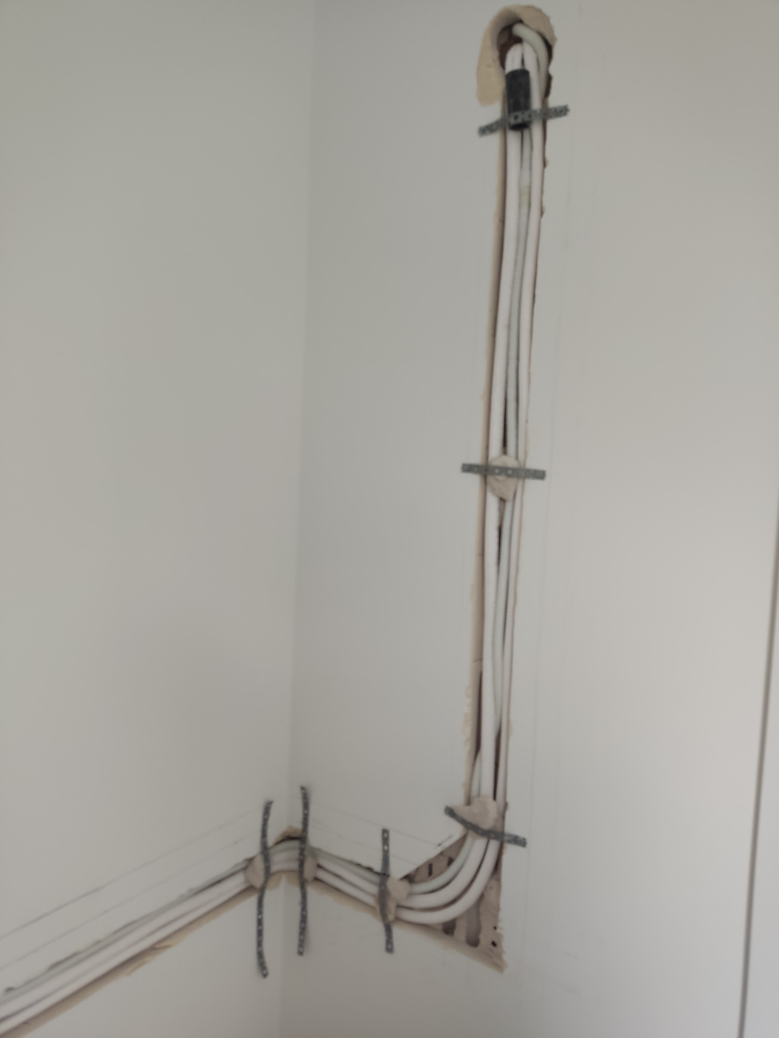 Białe przewody klimatyzacji zamocowane w ścianie za pomocą metalowych uchwytów. Instalacja w trakcie montażu, widoczne ślady po kuciu.