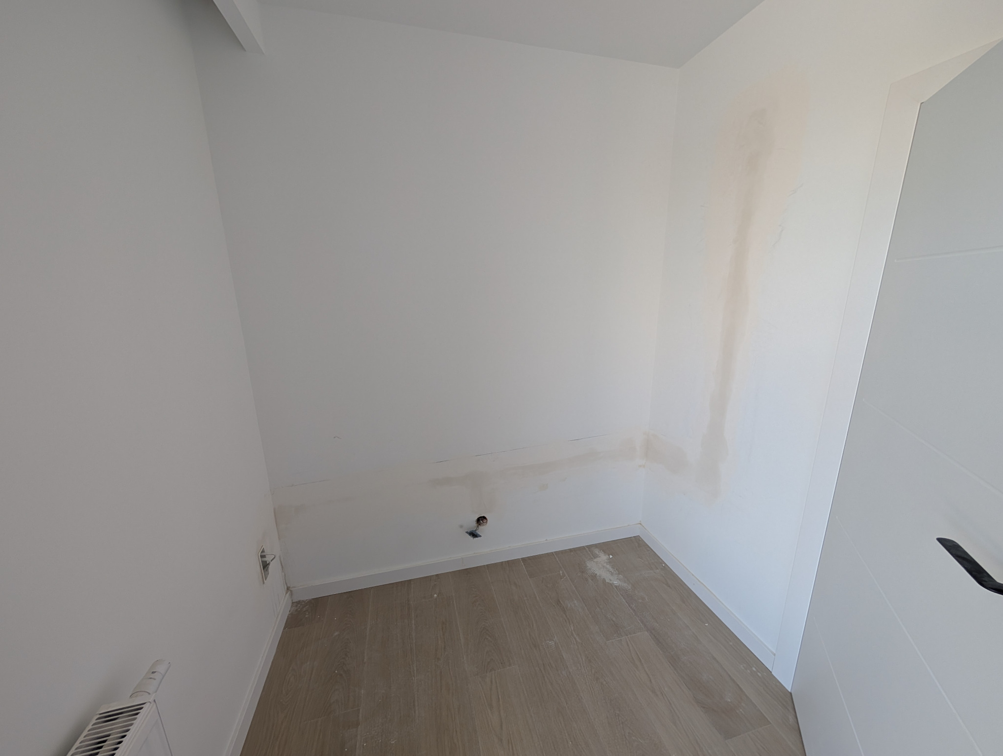 Przygotowanie pomieszczenia: ściany po szpachlowaniu, widoczne ślady po instalacji klimatyzacji, podłoga częściowo zakryta. Gotowe do dalszych prac wykończeniowych.