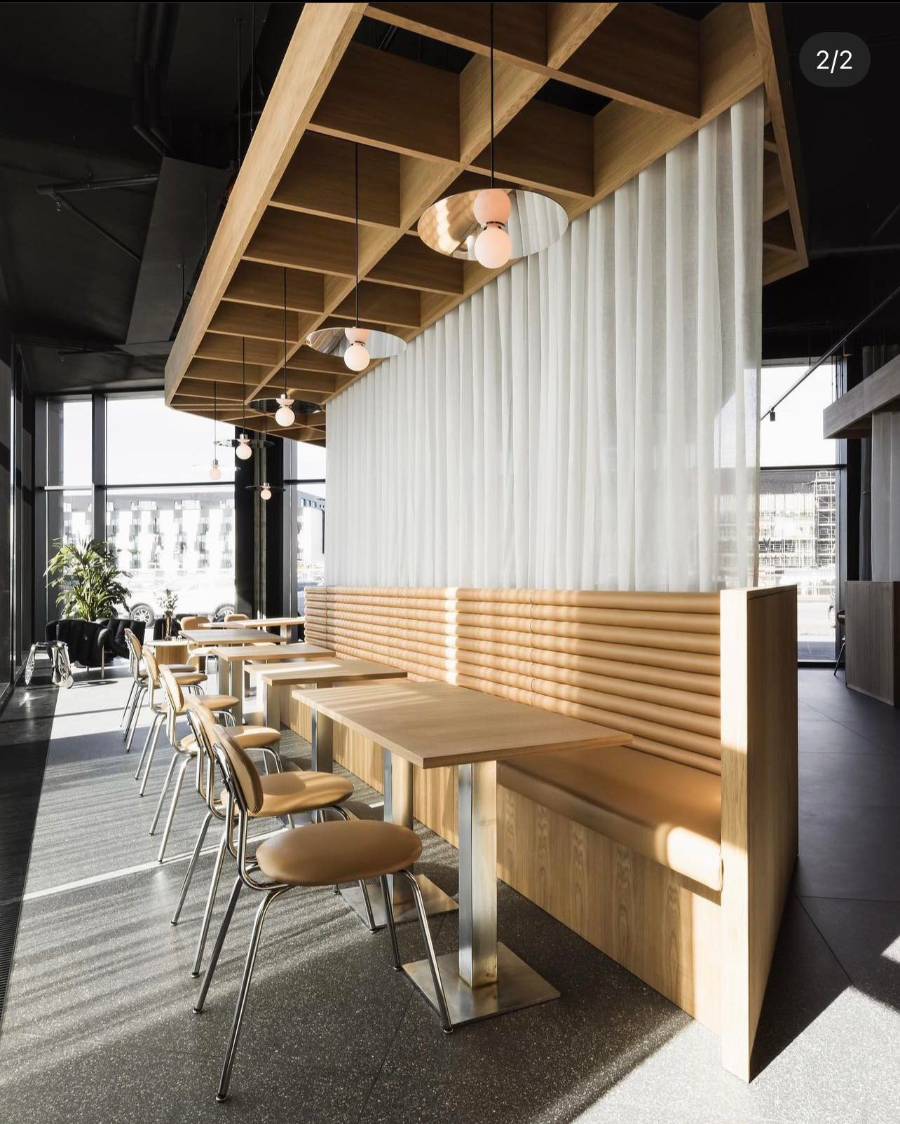 Jasne, zwiewne zasłony panelowe dzielące przestrzeń restauracji. Naturalne światło podkreśla minimalistyczny design z drewnianymi elementami i metalowymi detalami.