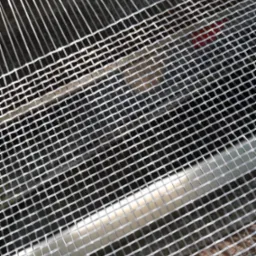 Siatka filtracyjna o drobnych oczkach, ukośnie ułożona, z widocznymi cienkimi, metalowymi prętami w tle. Element studni głębinowej.