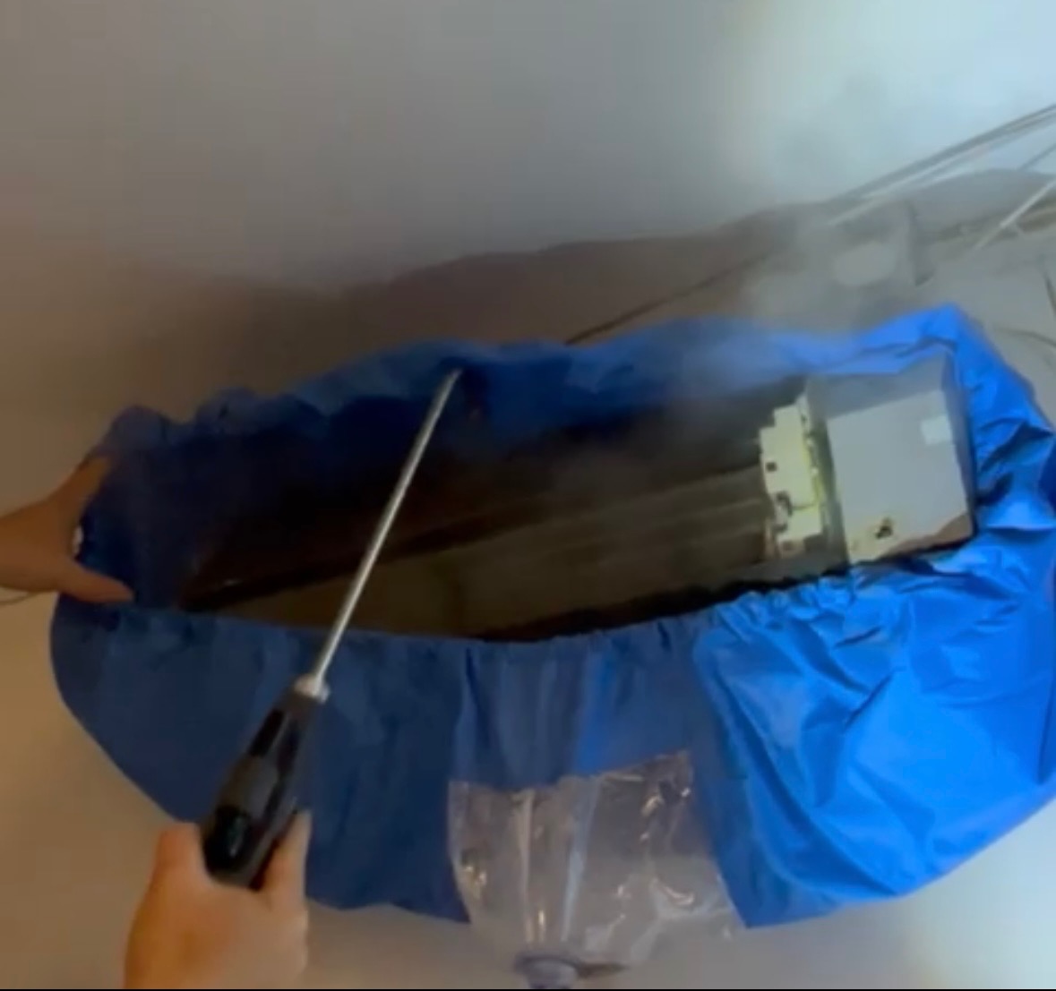 Czyszczenie klimatyzacji z użyciem specjalnej osłony i lancy. Para wodna wydobywająca się spod osłony. Widoczne elementy klimatyzatora i fragment dłoni.