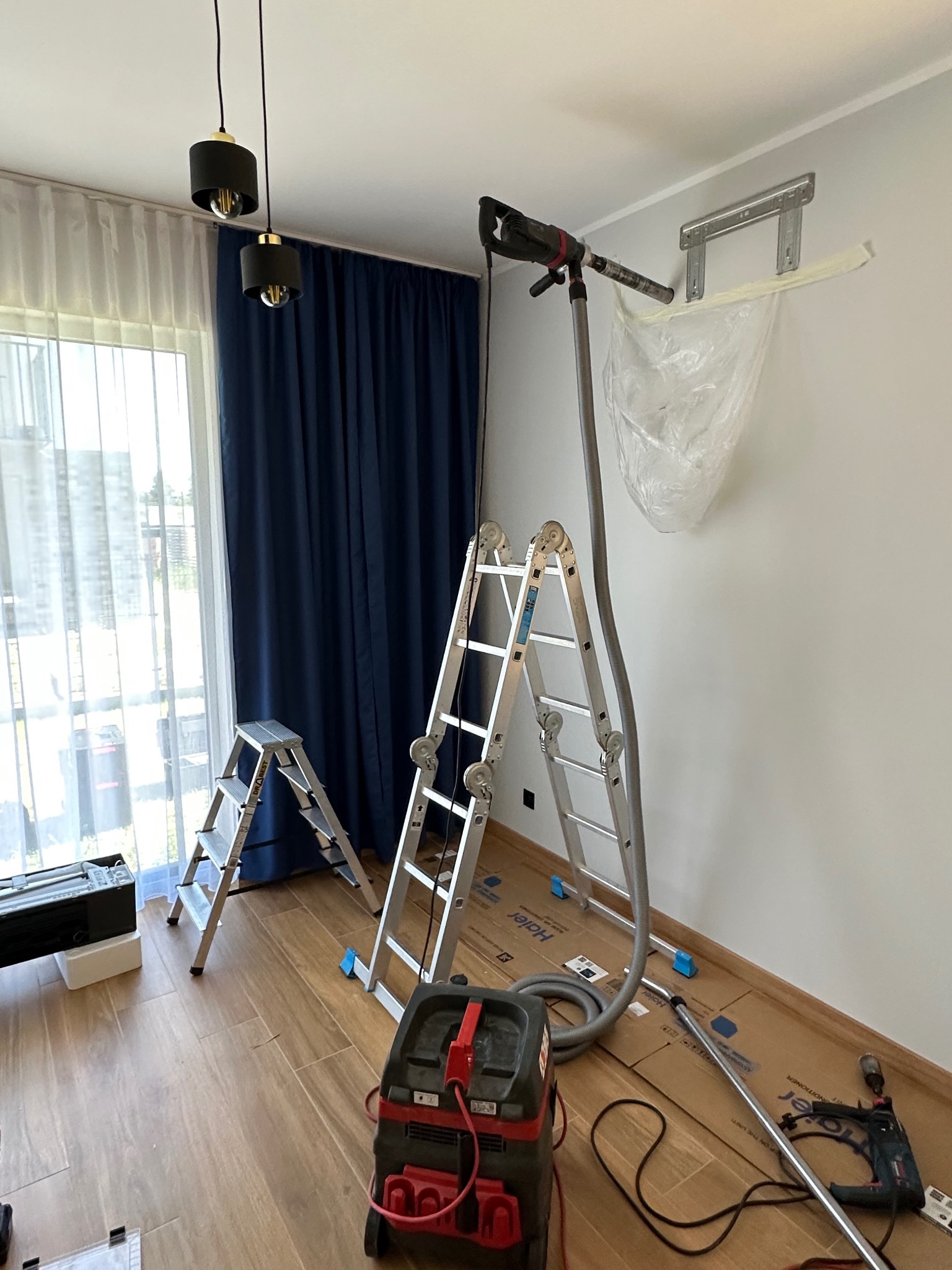 Montaż klimatyzacji w domu: drabiny, odkurzacz i narzędzia przygotowane do instalacji jednostki wewnętrznej na ścianie z niebieskimi zasłonami.