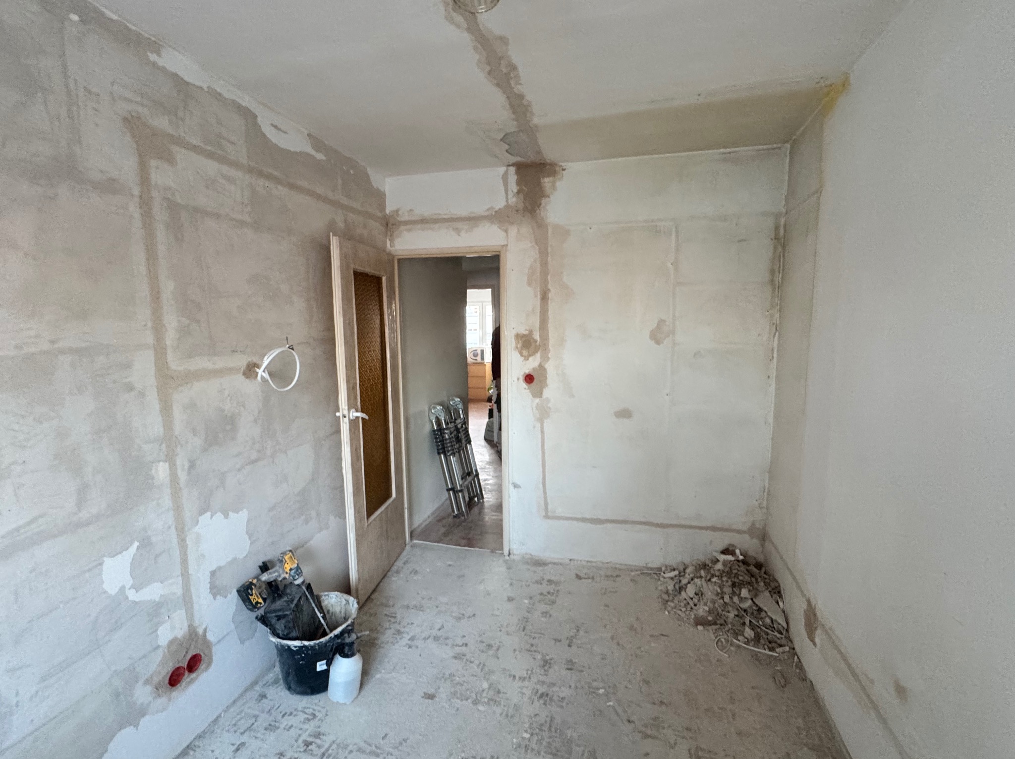 Remont pokoju: ściany w szpachli, widoczne kable elektryczne, narzędzia w wiadrze. Przygotowanie do malowania, widoczne ślady po instalacjach.