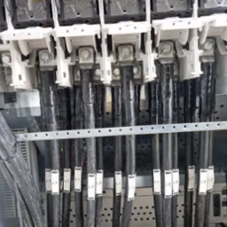 Szczegółowe ujęcie podłączenia przewodów elektrycznych w rozdzielni, z wyraźnie oznaczonymi fazami L1, L2, L3. Widoczne zaciski i metalowa konstrukcja szafy.