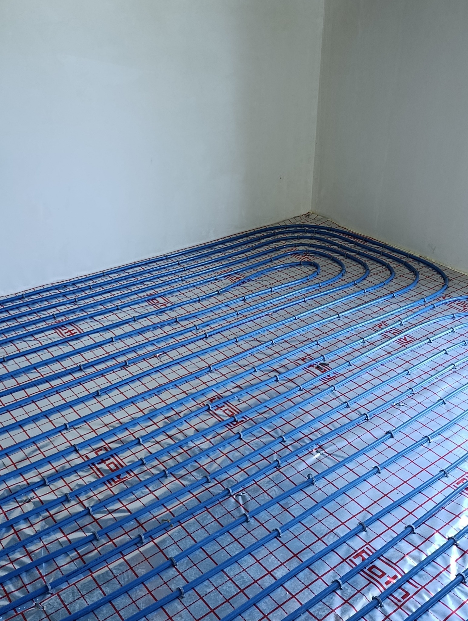 Instalacja ogrzewania podłogowego z rurami w kolorze niebieskim na folii aluminiowej, widok z góry w pomieszczeniu w Dobczycach.