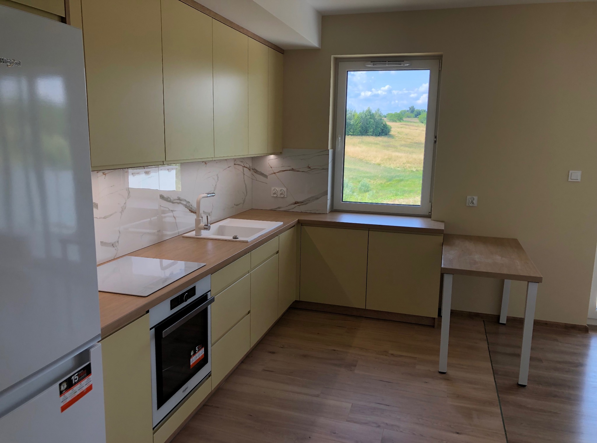 Jasna kuchnia na wymiar z drewnianym blatem i widokiem na zielony krajobraz za oknem. Nowoczesny design, minimalistyczny styl.