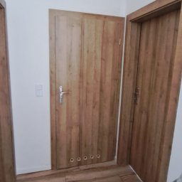 Łukasz Wilaszek - Wnętrze po montażu dwóch drewnopodobnych drzwi z widoczną podłogą w panelach. Na jednej z nich widoczne otwory wentylacyjne.