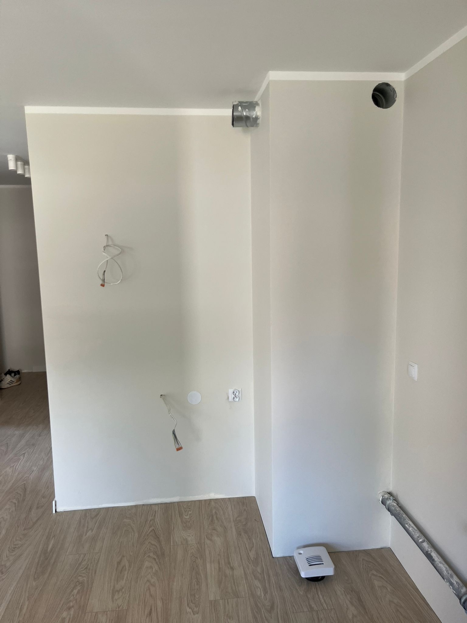 Jasne wnętrze w trakcie wykańczania: widoczne kable, otwory wentylacyjne, listwy przypodłogowe i panele podłogowe. Świeżo pomalowane ściany w odcieniach beżu.