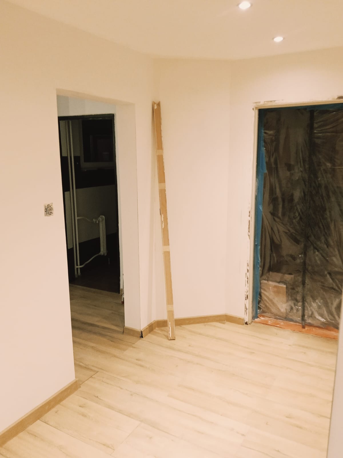 Jasne panele podłogowe w nowym mieszkaniu, ściany pomalowane na biało, drzwi zabezpieczone folią malarską, listwa przypodłogowa zamontowana.