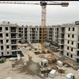 OLEH STOLIAR DOM BUD - Wysoka perspektywa na budowę wielopiętrowego budynku z betonu komórkowego. Na pierwszym planie widoczny sprzęt budowlany i dźwig na tle pochmurnego nieba.