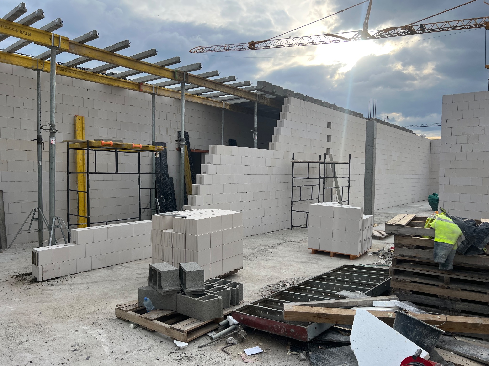 Budowa domu: ściana z białych bloczków, widoczne rusztowania i dźwig w tle. Częściowo wzniesiona konstrukcja budynku w słoneczny dzień.