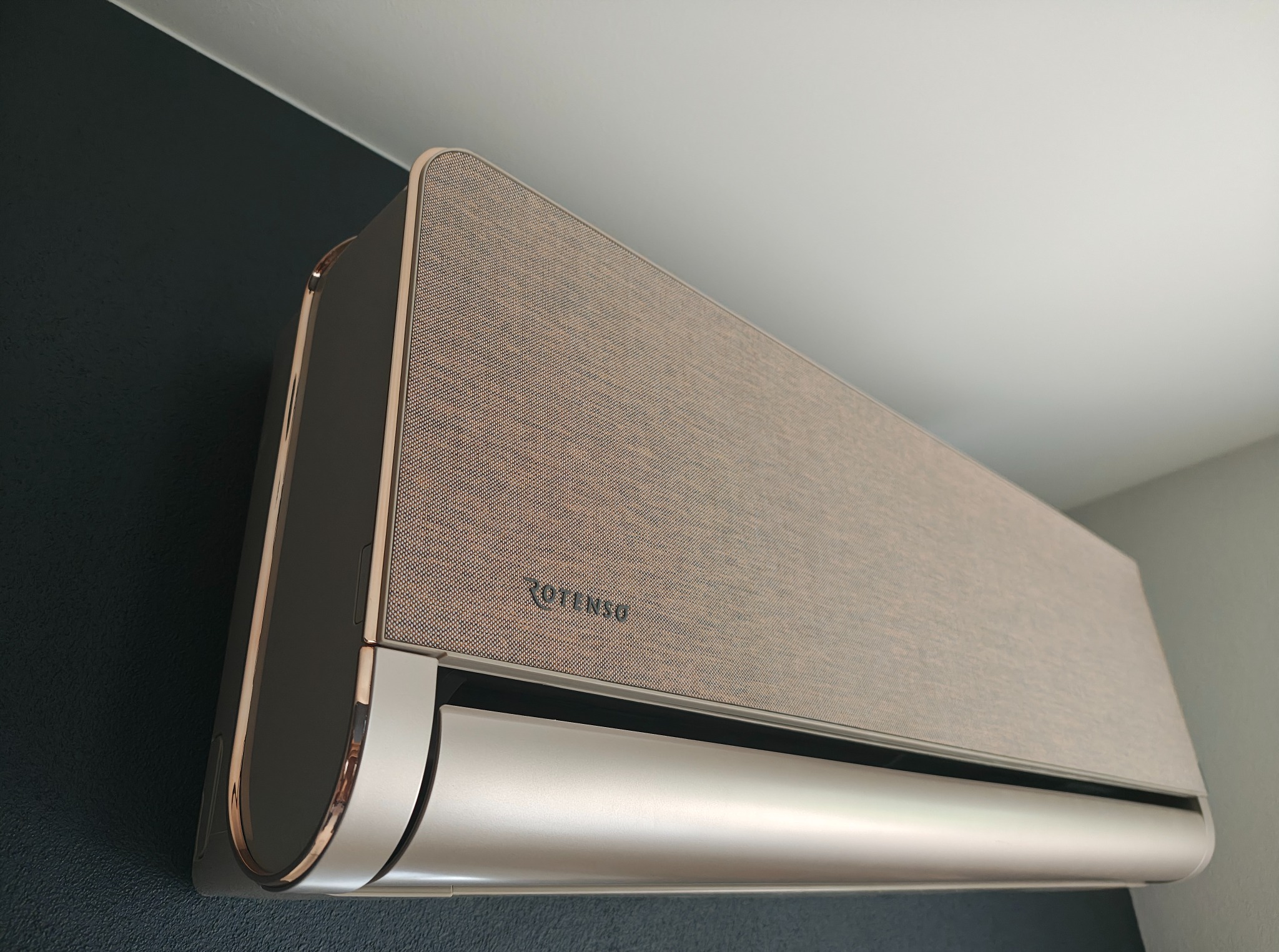 Elegancki klimatyzator Rotenso w odcieniach beżu i srebra, zamontowany na ścianie w pomieszczeniu. Widok z dołu, podkreślający nowoczesny design urządzenia.