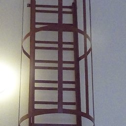 Tatorex - Metalowa drabina ewakuacyjna z zabezpieczeniem w postaci kosza ochronnego, zamontowana na ścianie wewnątrz budynku.