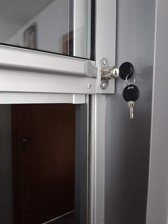 Detal metalowych drzwi z zamkiem cylindrycznym i pękiem kluczy, widok z bliska na zamek i fragment skrzydła drzwiowego.