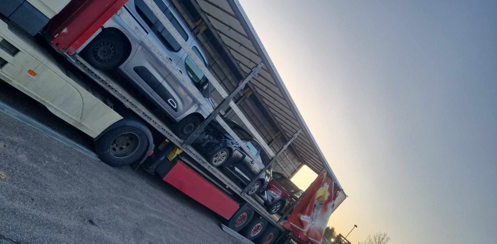 Laweta z trzema samochodami osobowymi różnych marek podczas transportu. Widok z dołu na ciężarówkę i niebo. Ujęcie z boku, lekko pod kątem.