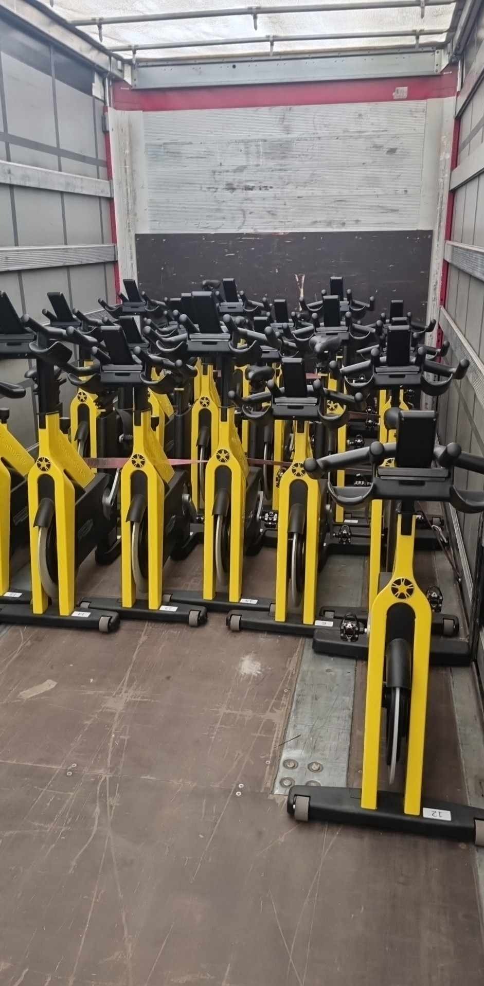 Wnętrze ciężarówki wypełnione rzędami żółto-czarnych rowerów stacjonarnych, ustawionych blisko siebie, gotowych do transportu. Widoczne detale konstrukcyjne pojazdu.
