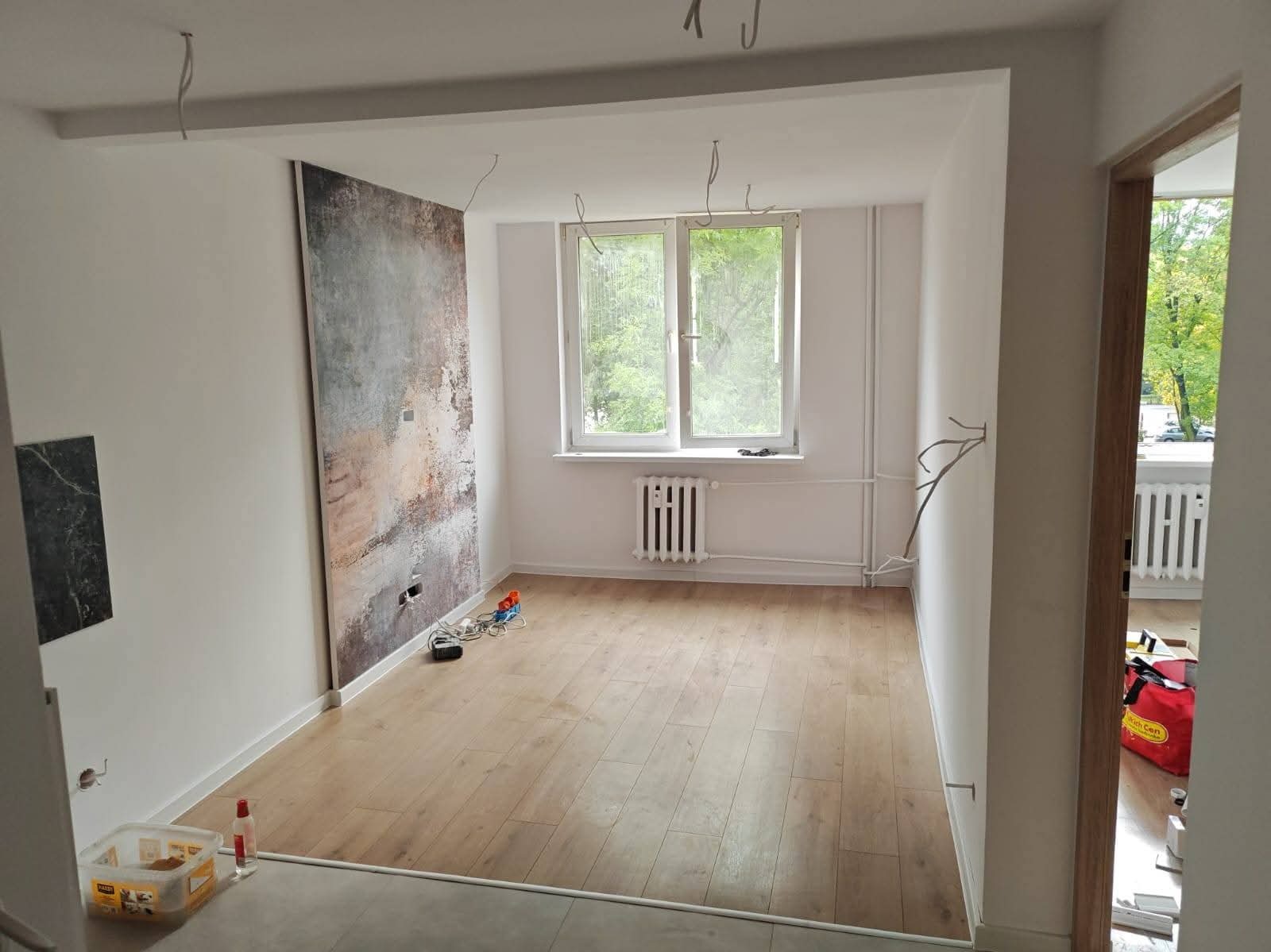 Wnętrze po remoncie w Radziszowie: świeżo pomalowane ściany, panele podłogowe, dekoracyjna ściana z fakturą. Widoczne przewody elektryczne, przygotowane do montażu oświetlenia.