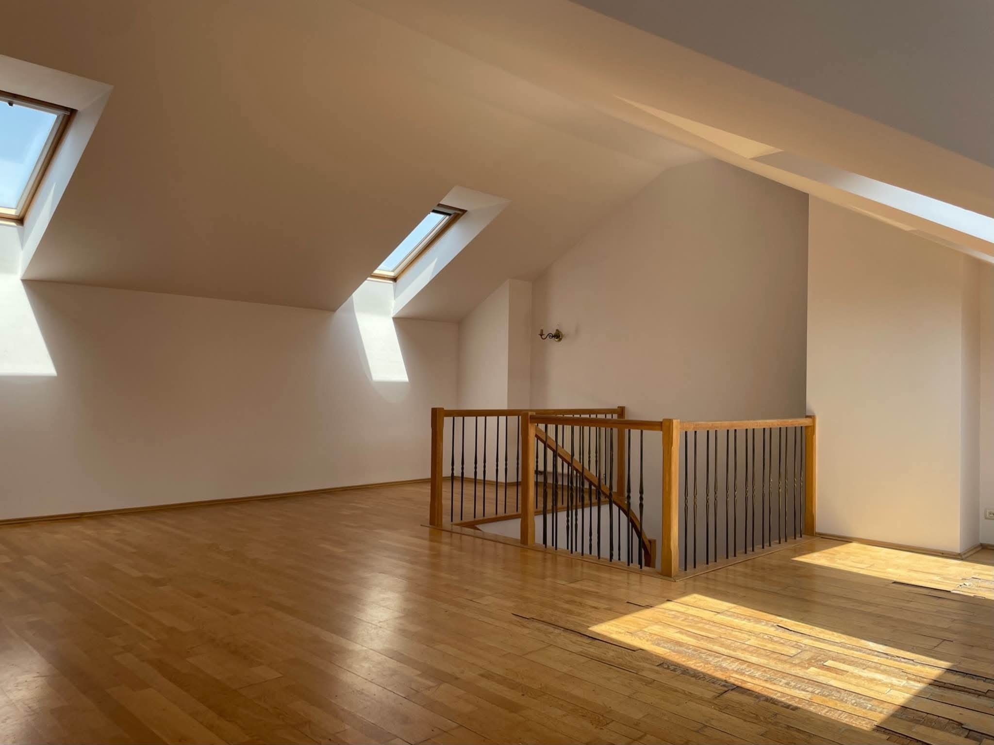 Poddasze z drewnianą podłogą i schodami, świeżo pomalowane na biało, z oknami dachowymi wpuszczającymi jasne światło słoneczne.