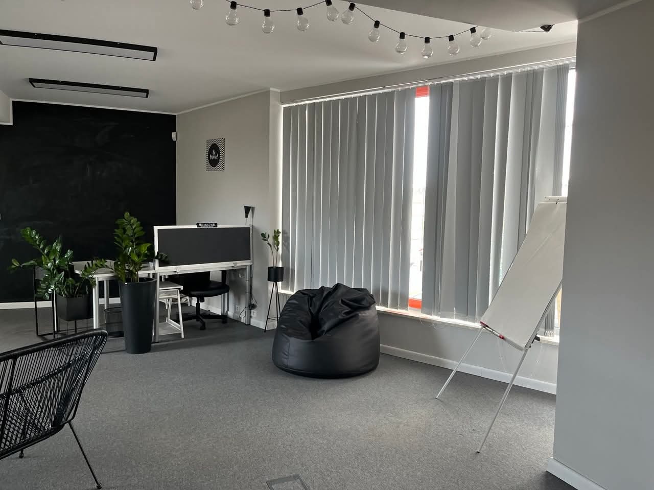 Nowoczesne biuro po malowaniu: czarna ściana tablicowa, szare ściany, minimalistyczne meble, rośliny doniczkowe i girlanda żarówkowa.