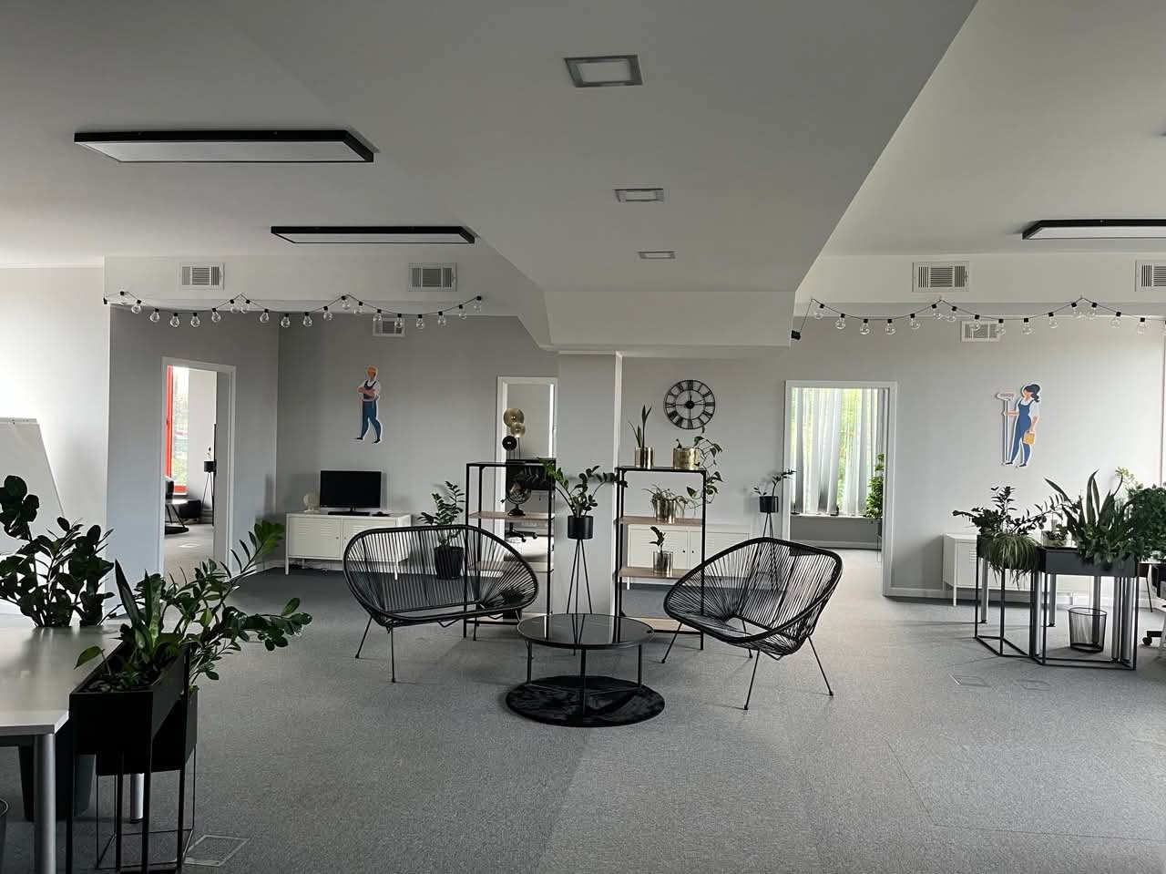 Jasne, przestronne biuro po malowaniu ścian na szaro, z dekoracyjnymi naklejkami postaci, roślinami i designerskimi meblami. Nowoczesne oświetlenie.
