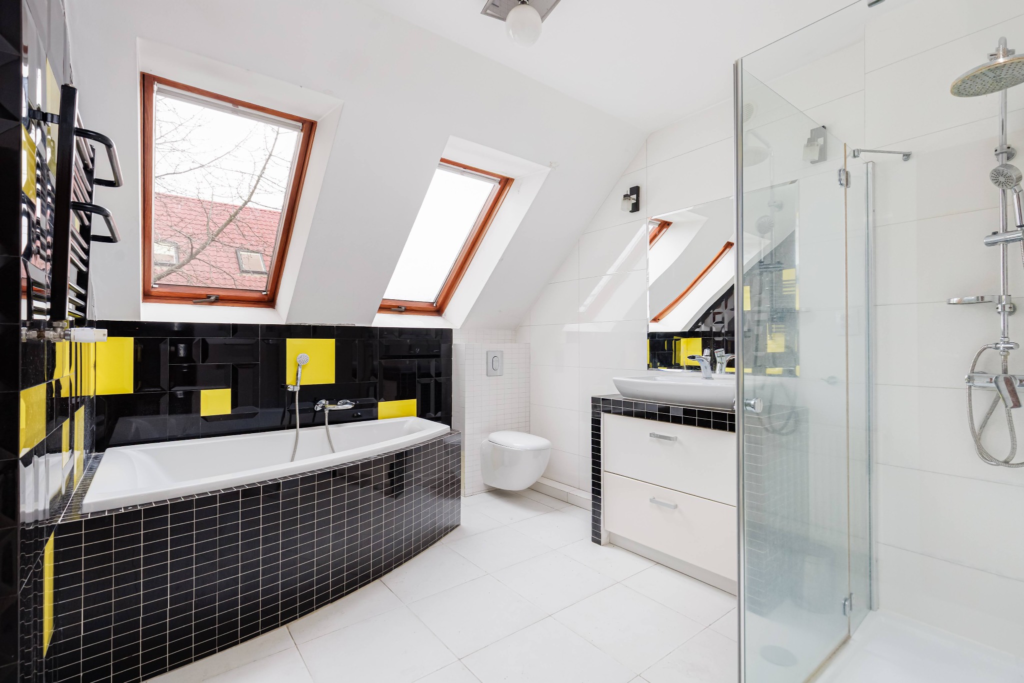 Nowoczesna łazienka na poddaszu z oknami dachowymi, czarno-żółtą mozaiką przy wannie i kabiną prysznicową ze szkła. Białe płytki i armatura tworzą jasne, przestronne wnętrze.