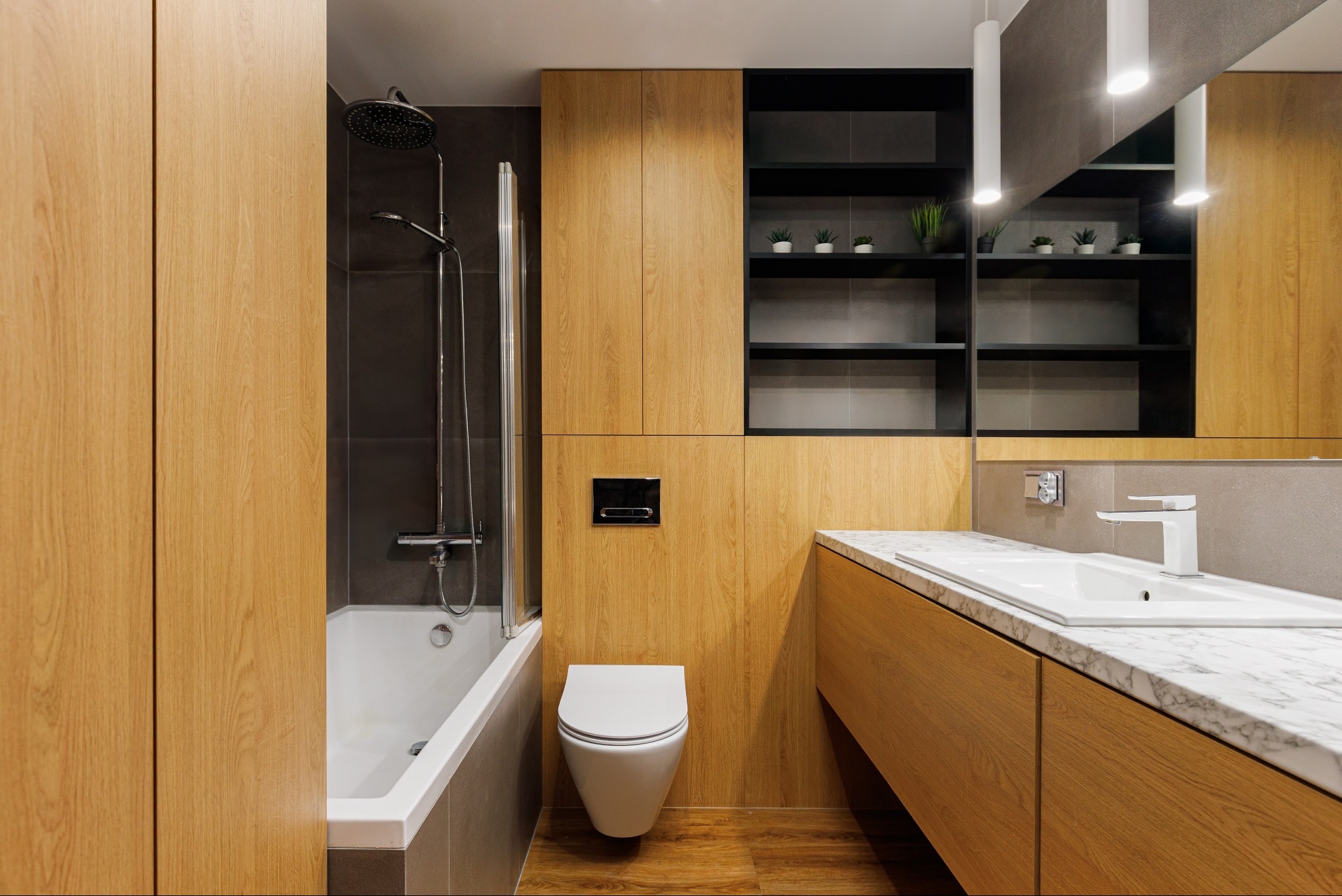 Nowoczesna łazienka z drewnianymi szafkami, białą armaturą i czarnymi półkami z roślinami. Minimalistyczny design, oświetlenie punktowe, marmurowy blat umywalki.