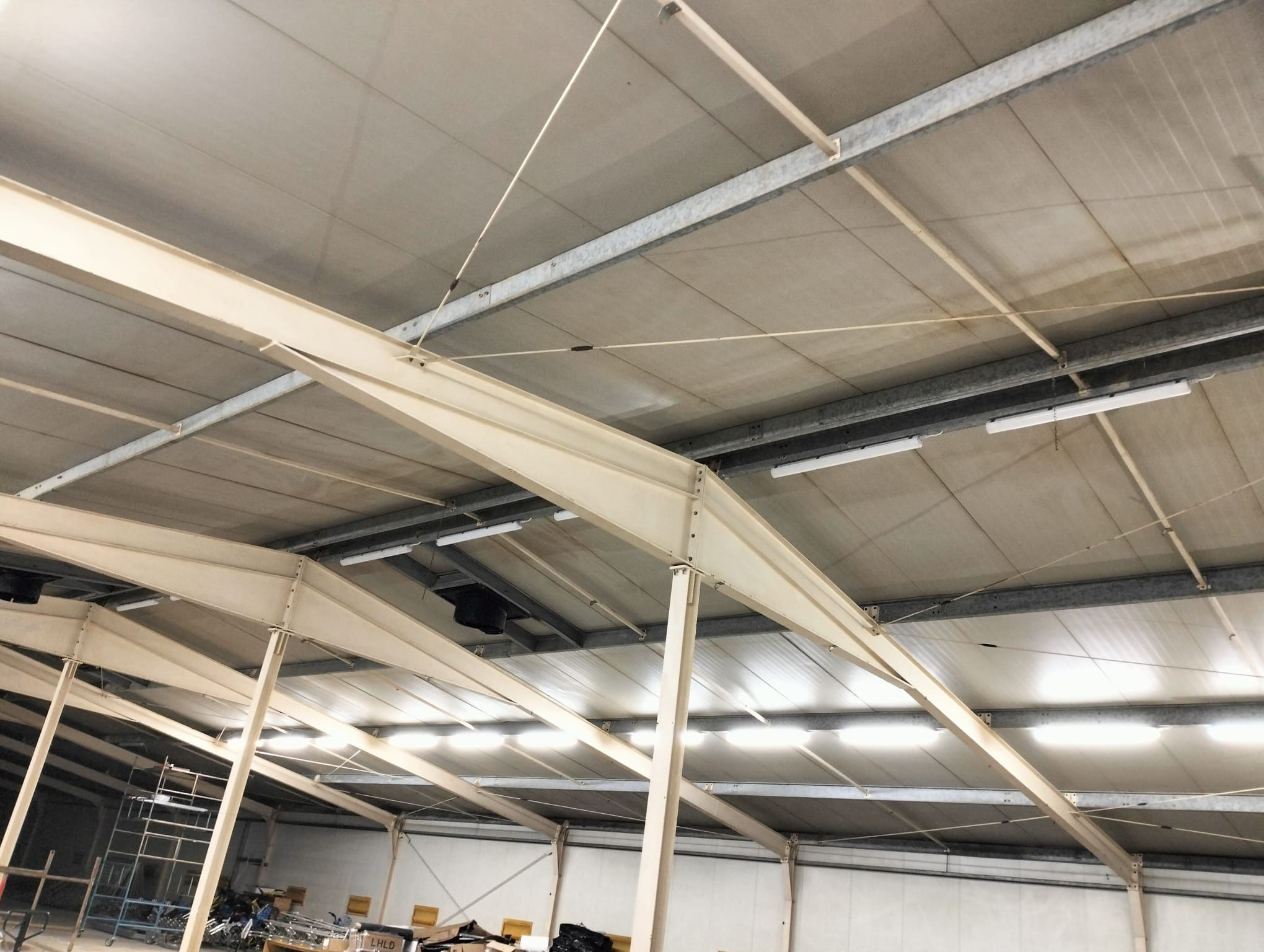 Wnętrze hali z widoczną konstrukcją stalową dachu, oświetleniem LED i elementami instalacji podwieszonymi do sufitu. Widoczne również elementy wyposażenia hali.