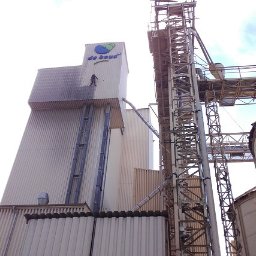 Dolomatex - Pracownik myje elewację przemysłową z logotypem na wysokości, widoczne metalowe konstrukcje i zbiorniki. Częściowo umyta powierzchnia kontrastuje z zabrudzoną.