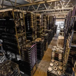 Magazyn opon i felg samochodowych, regały wypełnione po brzegi, widok z góry, metalowa konstrukcja dachu, oświetlenie magazynowe.