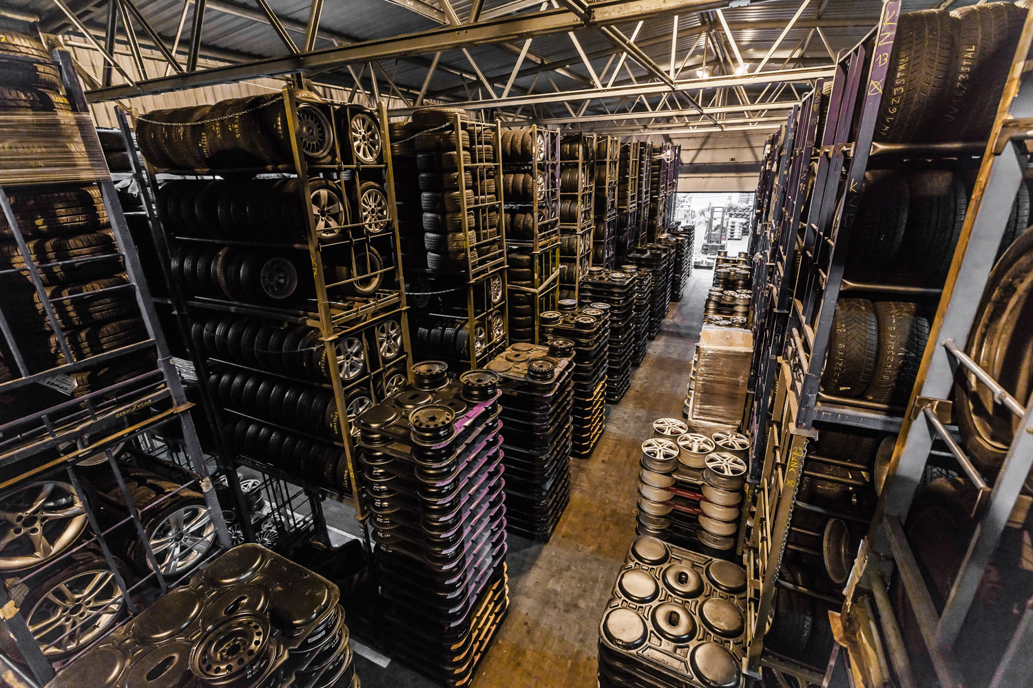 Magazyn opon i felg samochodowych, regały wypełnione po brzegi, widok z góry, metalowa konstrukcja dachu, oświetlenie magazynowe.